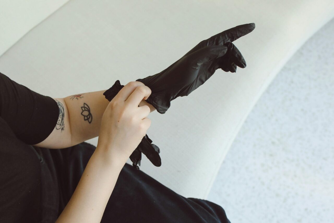 A person with a tattoo puts on black latex gloves, focusing on hand safety.
